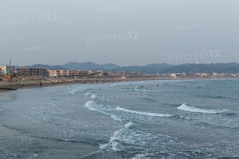 Houses on the seafront and surfers in the surf at dusk on the beach in Kamakura, Kanagawa Prefecture, Japan