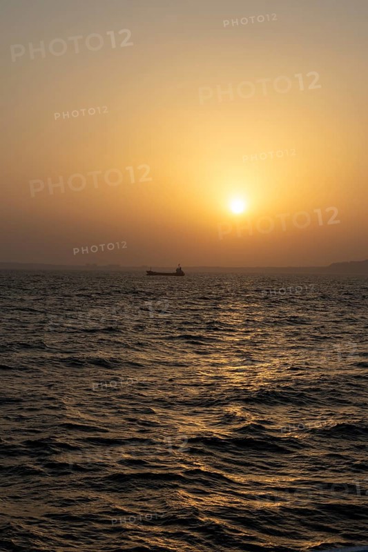 Background image, setting sun with silhouette of ship and land, water surface in evening light, waves in the sea at sunset, Tokyo Bay, Japan