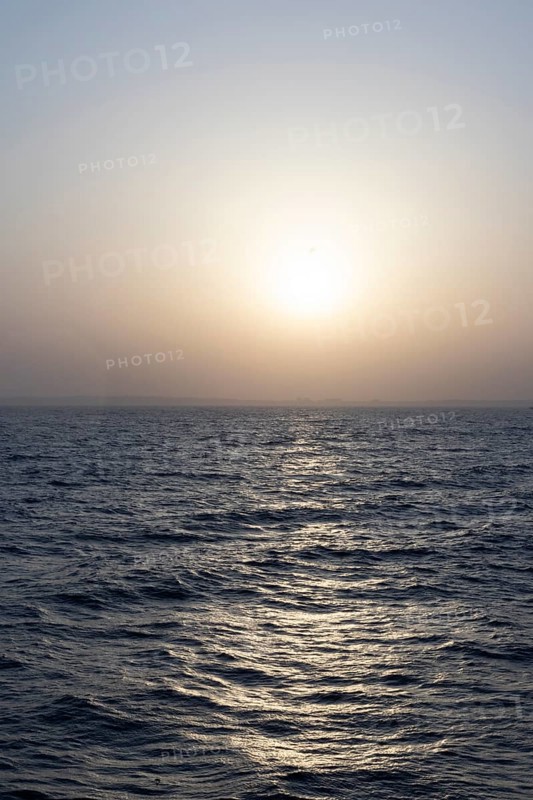 Background image, setting sun with silhouette of land, water surface in evening light, waves in the sea at sunset, Tokyo Bay, Japan
