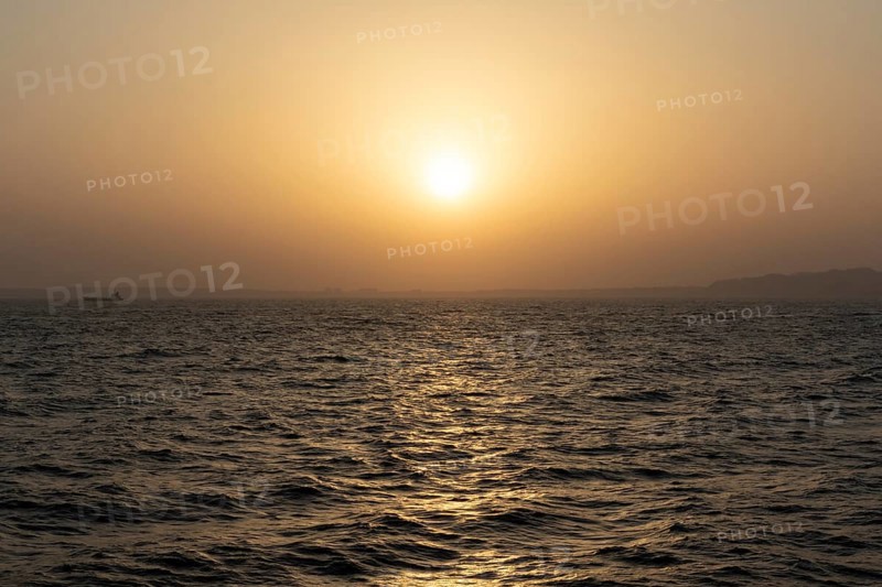 Background image, setting sun with silhouette of land, water surface in evening light, waves in the sea at sunset, Tokyo Bay, Japan