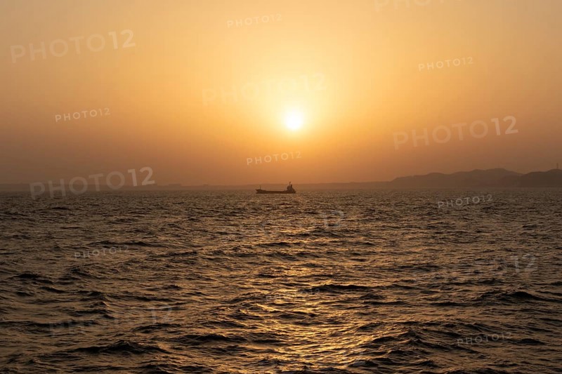 Background image, setting sun with silhouette of ship and land, water surface in evening light, waves in the sea at sunset, Tokyo Bay, Japan