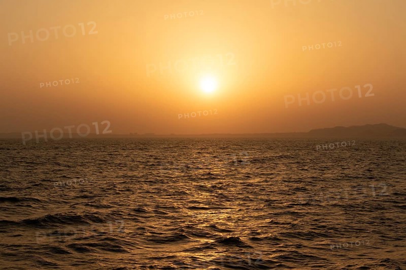 Background image, setting sun with silhouette of land, water surface in evening light, waves in the sea at sunset, Tokyo Bay, Japan