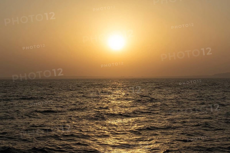 Background image, setting sun with silhouette of land, water surface in evening light, waves in the sea at sunset, Tokyo Bay, Japan