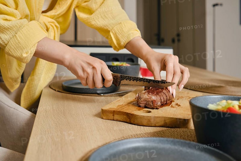 A person skillfully slices a perfectly cooked duck breast on a wooden cutting board in a stylish kitchen. Fresh vegetables sit in bowls nearby, indicating a nutritious meal being prepared
