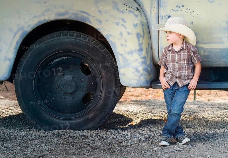 Young boy wearing cowboy hat relaxing leaning against antique truck