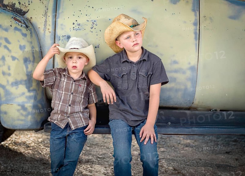 Two young boys wearing cowboy hats leaning against antique truck