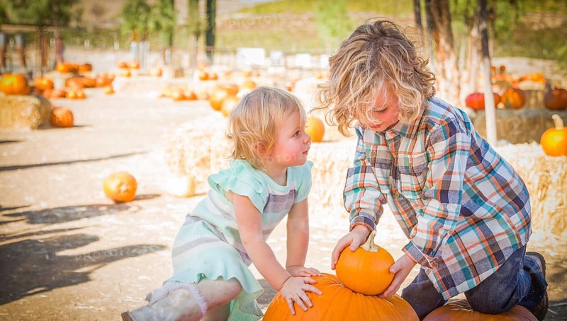 Young brother and sister playing in a rustic ranch setting at the pumpkin patch
