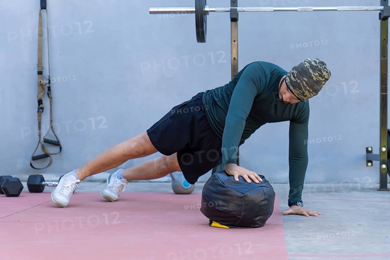 Focused male athlete wearing a beanie performing one-handed push-ups on a medicine ball in an outdoor gym, showcasing strength and dedication to fitness
