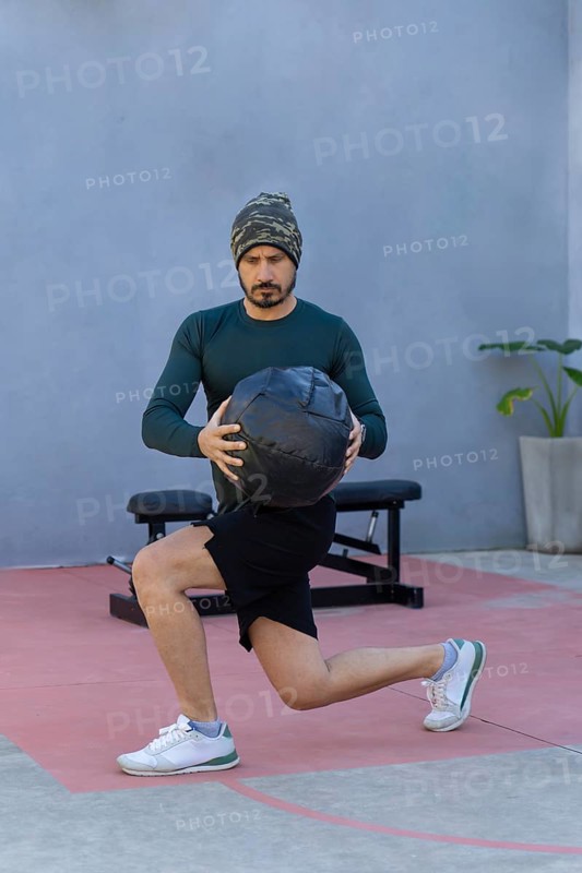 Athlete performing lunges while gripping a medicine ball, showcasing strength and balance during an invigorating outdoor workout, embodying a commitment to fitness and wellness