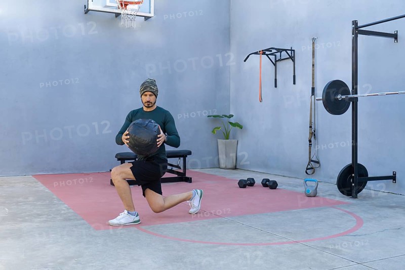 Athlete is performing lunges while holding a medicine ball in an outdoor gym, showcasing strength and balance during his workout routine