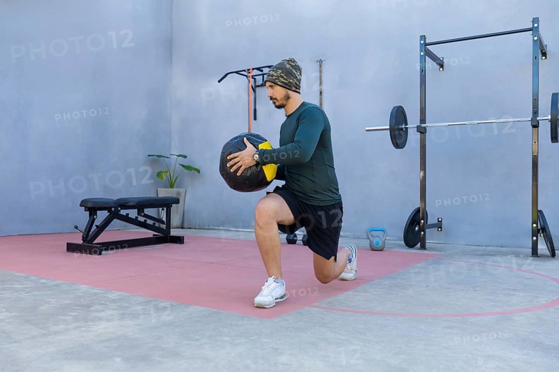 Athlete performing lunges while gripping a medicine ball in an outdoor gym, demonstrating strength and balance during an intense workout session focused on fitness and endurance