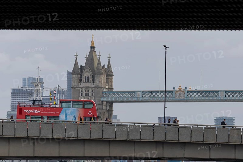 Red double decker bus driving over a bridge with Tower bridge in the background, City of London, England, United Kingdom