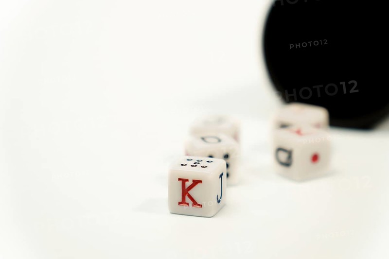 Poker dice showing king, jack, queen and ten on white background with black cup