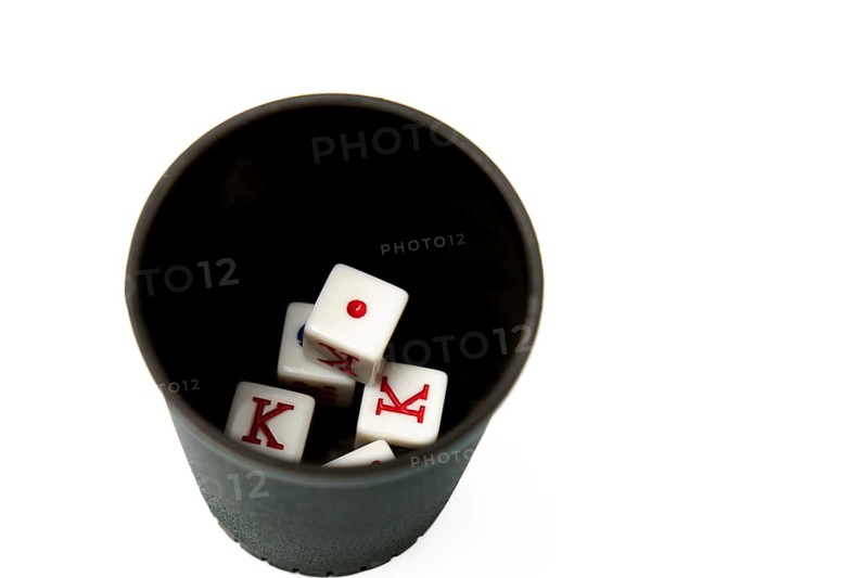 Four white dice showing king and one resting in a black dice cup on a white background, suggesting gambling and games of chance
