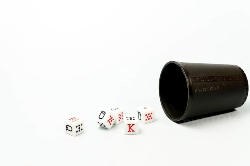 White poker dice with red and black markings rolling out of dark brown dice cup on white background