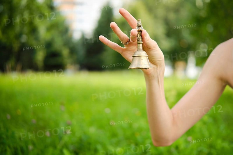A hand gracefully holds a singing bell in a vibrant green garden, with soft sunlight filtering through nearby trees. The tranquil setting enhances the calming energy of the bowl