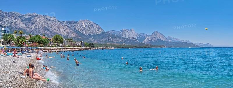 KEMER, TURKEY - JULY 5, 2025 Kemer municipality public beach with vibrant pebble under a clear, turquoise sea water. People swimming and sunbathing on the shore. Beautiful Taurus mountains at horizon