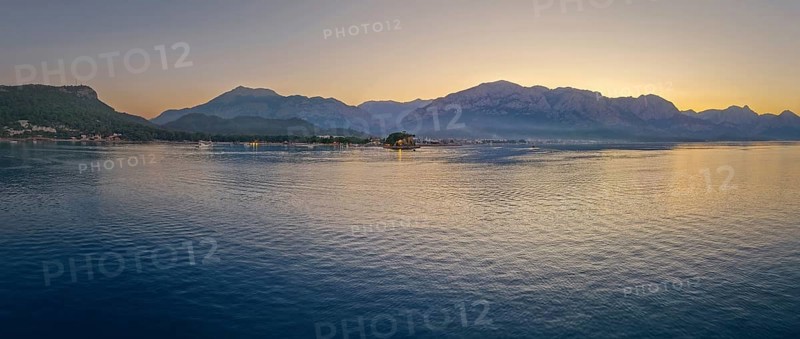 Panoramic dusk scene in Kemer, Turkey, showing the town illuminated coastline and beach, reflected beautifully on the calm sea. Majestic Taurus mountains silhouettes in the background