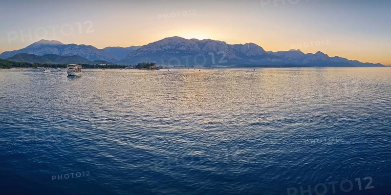 Seascape sunset panorama over the Mediterranean Sea near Kemer, Turkey. Panoramic view to the moonlight beach at dusk and the majestic Taurus mountains in the background