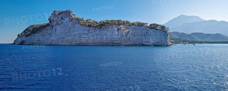 Vibrant seascape panorama with beautiful Turkish mediterranean coastline lined with tree covered cliffs and hills under a clear sky in Kemer, Turkey
