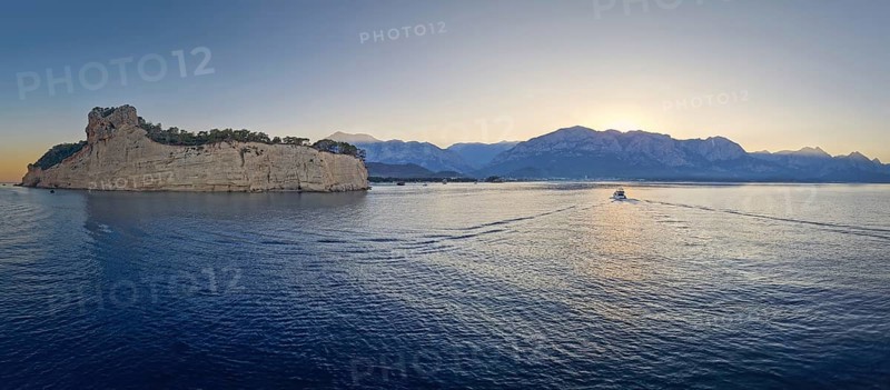 Scenic sunset panorama over Turkish Mediterranean coastline, with majestic Taurus mountains in the background. Boat sailing on the calm sea water in Kemer, Turkey