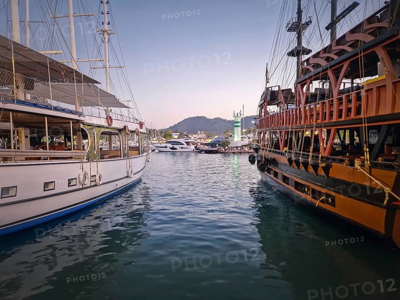 Kemer marina at dusk, filled with multiple docked boats. Lights of the harbor and the resort shoreline reflects on the calm sea water