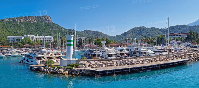 KEMER, TURKEY - JULY 3, 2025 Marina panoramic view with Calis Hill in the background. Rocky pier filled with numerous boats and yachts on the clear turquoise water under a bright blue Turkish sky