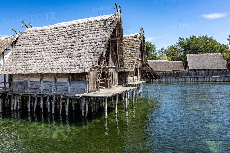 Traditional stilt house towers over shimmering green water in tranquil surroundings, Lake Dwellings Unteruhldingen Open-Air Museum Lake Constance Germany