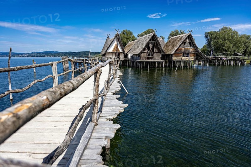 Wooden walkway leads to traditional stilt houses surrounded by calm water, pile dwellings Unteruhldingen Open-Air Museum Lake Constance Germany