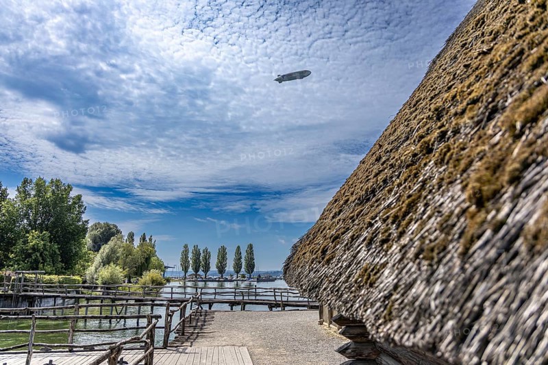 Thatched roof building with a view of trees and clouds in a rural setting, pile dwellings Unteruhldingen Open-Air Museum Lake Constance Germany