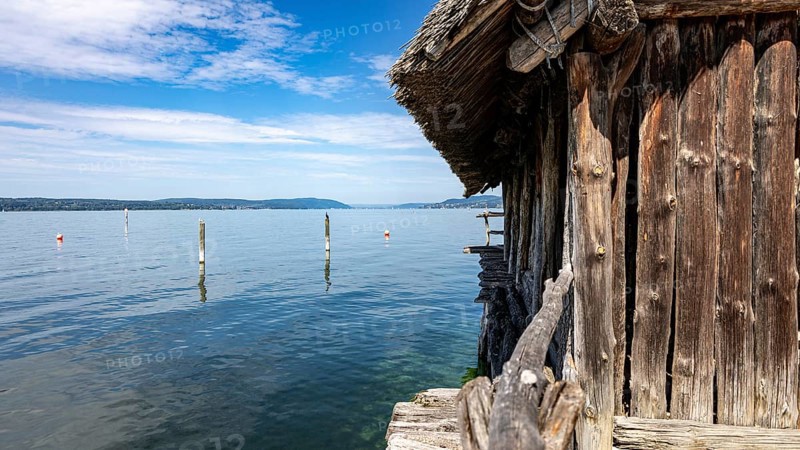 Wooden hut directly on the lake with blue sky and scattered clouds, pile dwellings Unteruhldingen Open Air Museum Lake Constance Germany