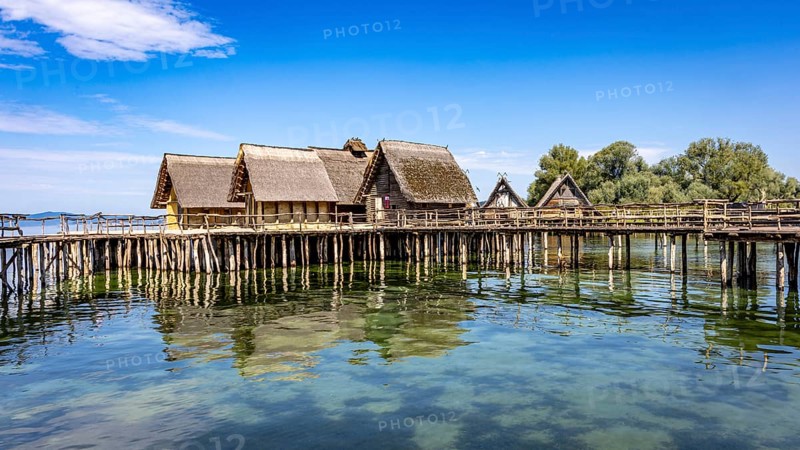 Historic pile dwellings on the shore of a lake with reflecting water, pile dwellings Unteruhldingen Open-Air Museum Lake Constance Germany