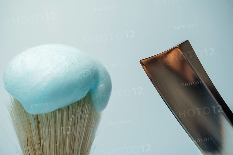 Shaving brush with light blue foam and metal razor blade ready for skincare routine