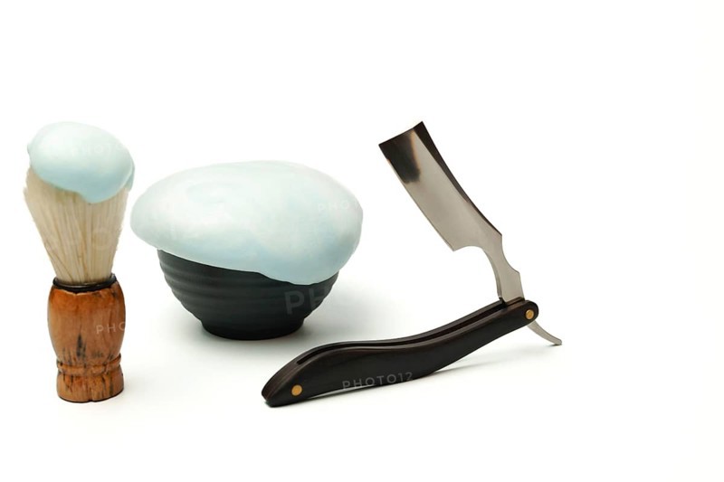 Shaving foam, brush, and straight razor are creating a grooming still life on a white background
