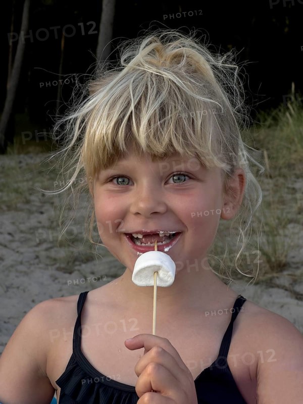 Happy blonde 7 year old Scandinavian girl eating marshmallows outdoors in Ystad, SkÃ¥ne County, Sweden, Scandinavian