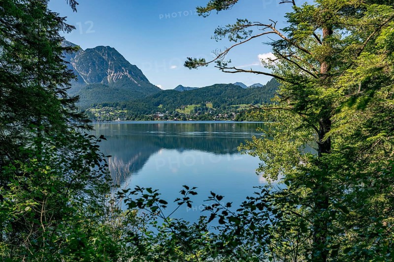 View of Lake Altaussee, framed by trees and mountains under a blue sky, Altaussee, Styria, Austria
