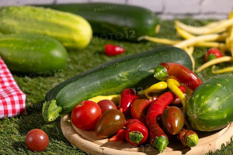 Fresh courgettes, tomatoes, cucumbers and peppers on a wooden board on grass