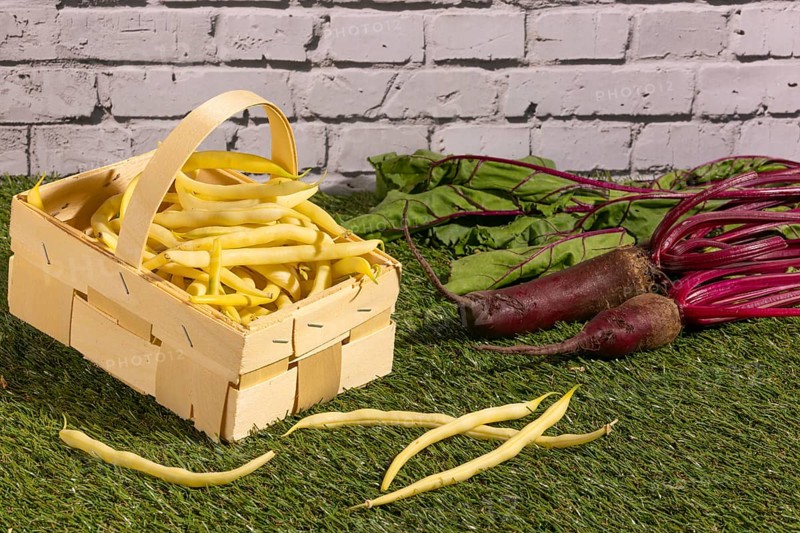 Basket with yellow beans and turnips on a green lawn in front of a wall