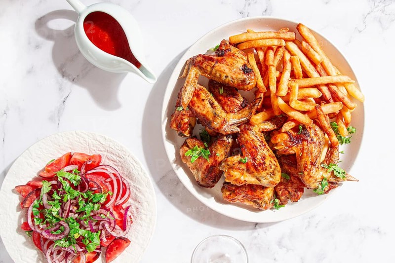 Delicious barbecue chicken wings, with French fries, salad and a refreshing drink, at a cozy table, there are no people