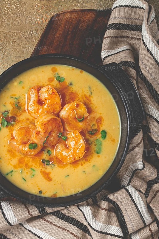 Creamy shrimp curry with spices, garnished with herbs, on a textured background, homemade, no people