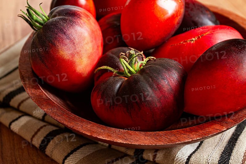 Freshly picked tomatoes, of the Black Beauty variety, in a wooden bowl, close-up, on the kitchen table