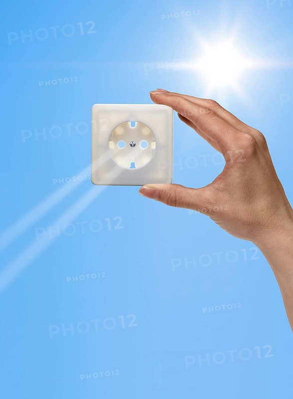 Symbolic solar energy theme showing the sun and sky with human hand holding a electrical socket while sunbeams falling through