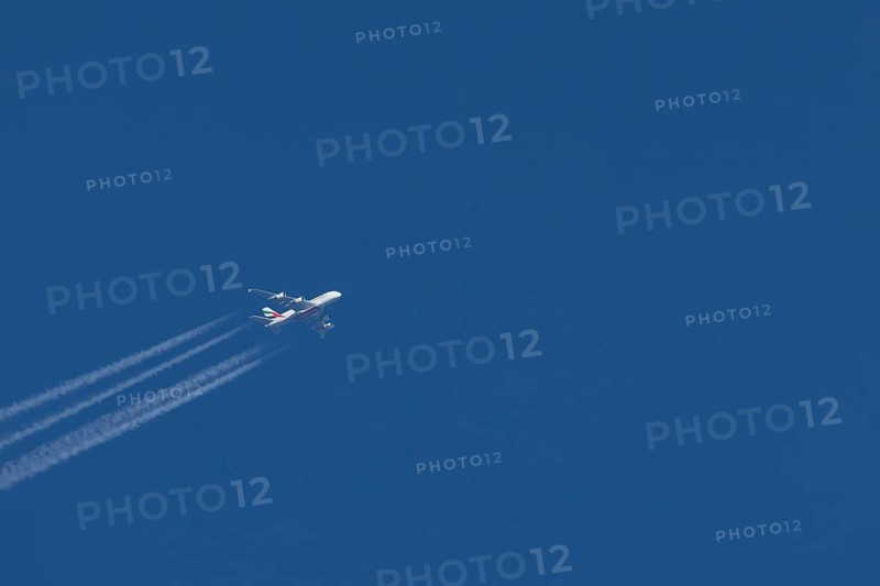 Airbus A380 jet passenger aircraft of Emirates airlines in flight in a blue sky with vapour trails or contrails behind, England, United Kingdom