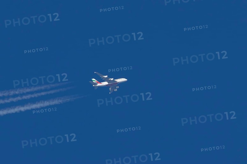 Airbus A380 jet passenger aircraft of Emirates airlines in flight in a blue sky with vapour trails or contrails behind, England, United Kingdom