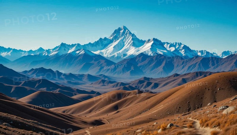 Majestic mountain range with snow-capped peaks, layered with rolling hills in shades of brown and blue under a clear sky, AI generated