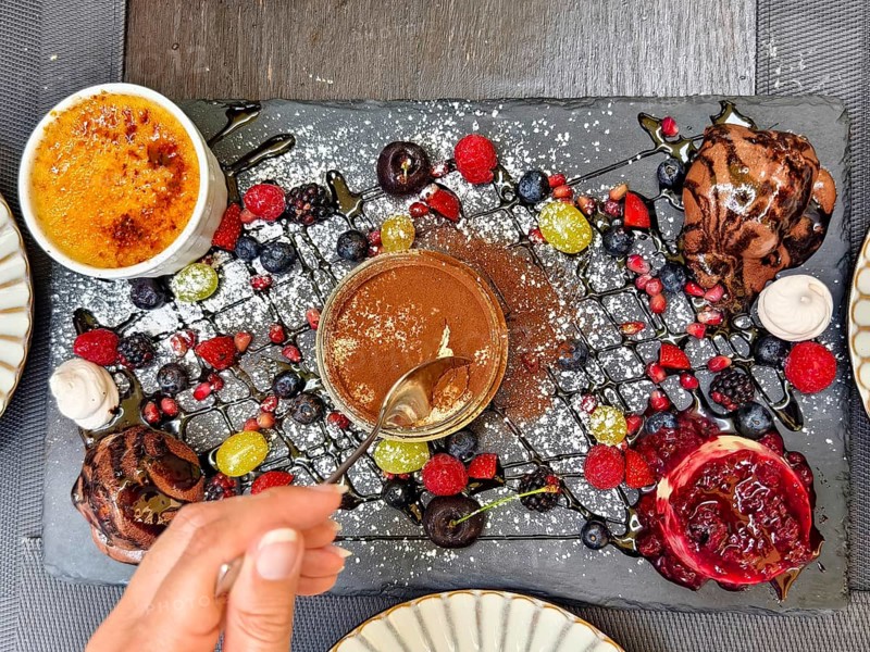 Hand with spoon tasting a dessert, surrounded by artfully arranged berries and chocolate Lower Austria Austria