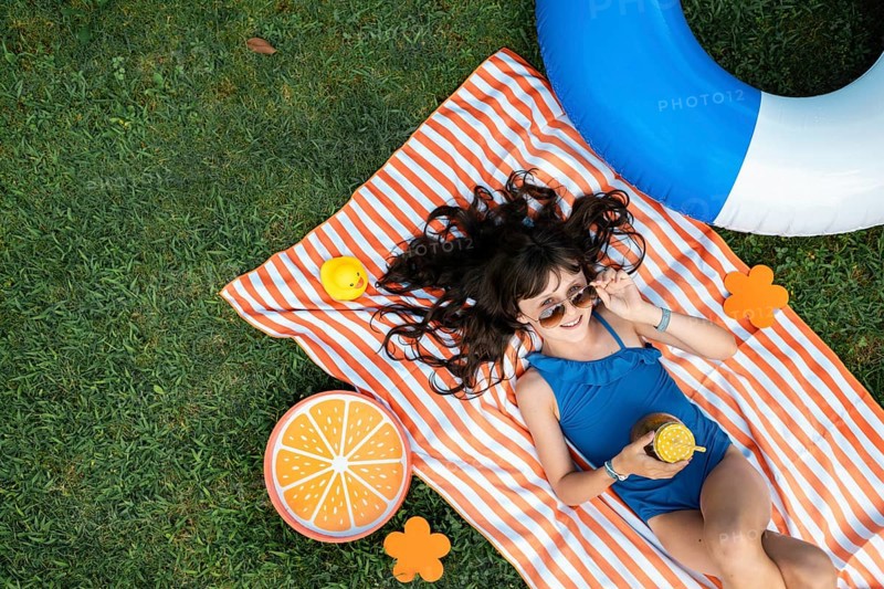 Girl, 10, with sunglasses in a blue swimming costume, lying relaxed in the meadow with a cocktail on a towel