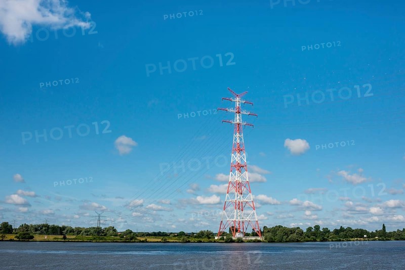 An extremely high electricity electricity electricity pylon, marked white and red, stands on the banks of the Elbe, river bank, Elbe crossing 2, 227 m high, highest overhead line pylon in Europe, surrounded by green landscape with trees and meadows under a blue sky, high-voltage pylon, overhead line pylon, overhead line, colour marking, safety, aviation safety, technology, structure, near Hollern-Twielenfleth, Lühe, Altes Land, Lower Saxony, Germany