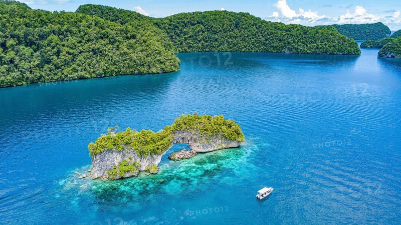 Aerial view bird's eye view of rock arch Natural Arch in lagoon of in island paradise island state Palau in the Pacific West Pacific, in front small boat with tourists, Rock Islands, Republic of Palau, Micronesia, Australia, Oceania