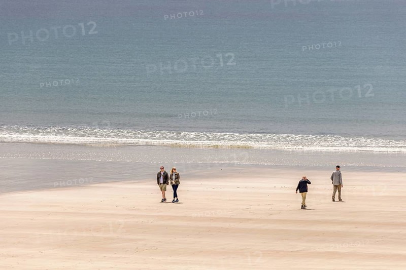 Group of people walking in the sunshine on a sandy beach with rolling waves at the sea, Crozon peninsula, Bretagne, France